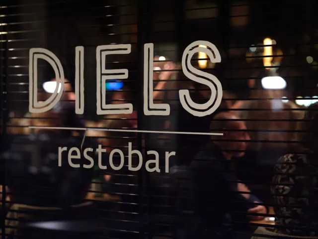 Het DIELS restobar-logo op het raam, met gasten erachter