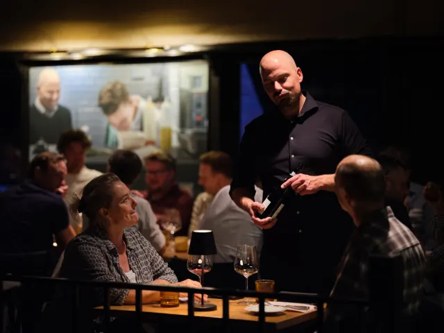 Elsko schenkt wijn aan tafel in de volle zaal